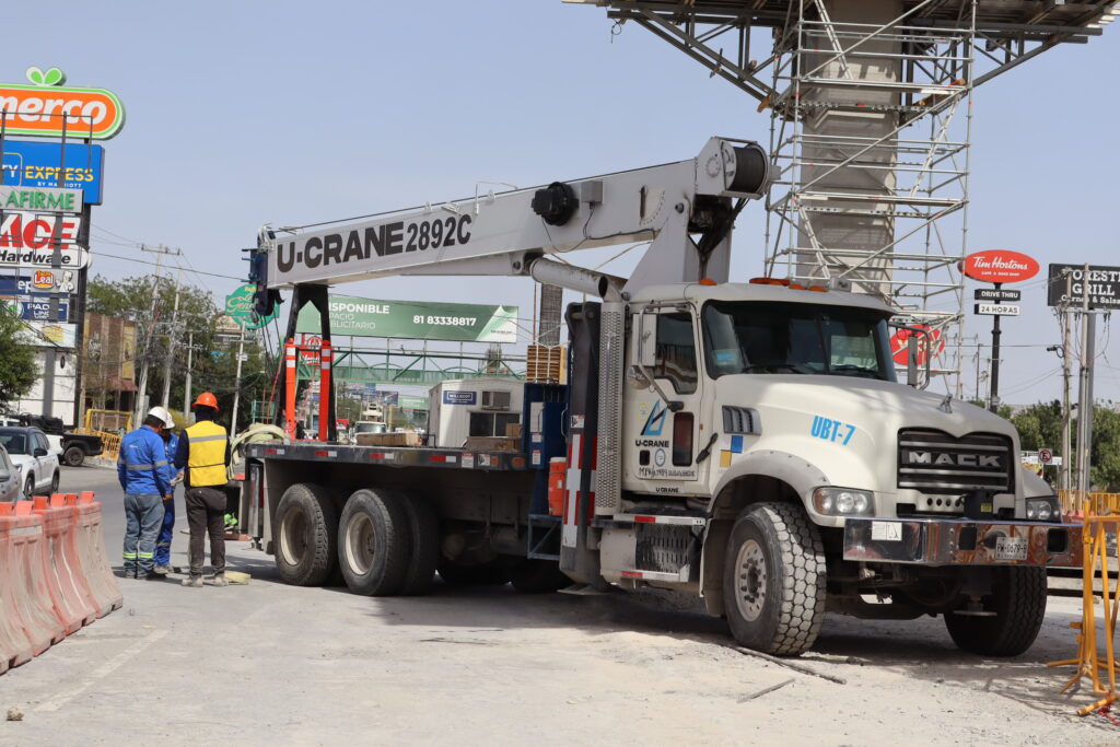 Camión grúa Mack Granite (U-CRANE 2892C) operando en una obra de construcción urbana. Esta maquinaria robusta y eficiente es esencial para el izaje de cargas pesadas, con personal capacitado y medidas de seguridad visibles. Imagen ideal para resaltar el uso de equipo pesado en proyectos de ingeniería y construcción.